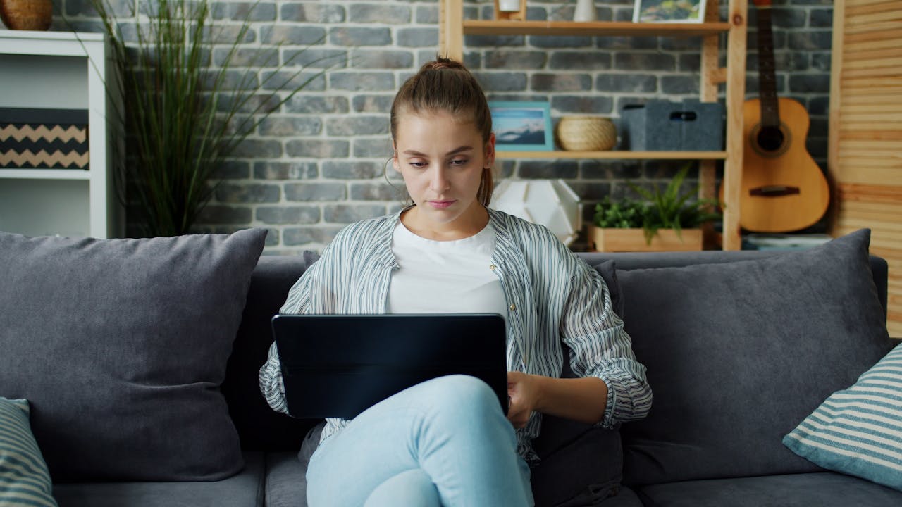 Young woman sitting on a sofa using a laptop in a home setting.